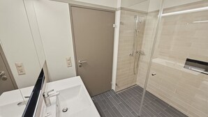 A bathroom with a white sink, a mirror, a shower with a glass door, and a tiled floor. - Comfortable 1BR flat / great location - Baron 44 (Zürich)