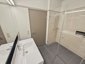 Uma casa de banho com uma pia branca, um espelho, um chuveiro com porta de vidro e chão em azulejo.
