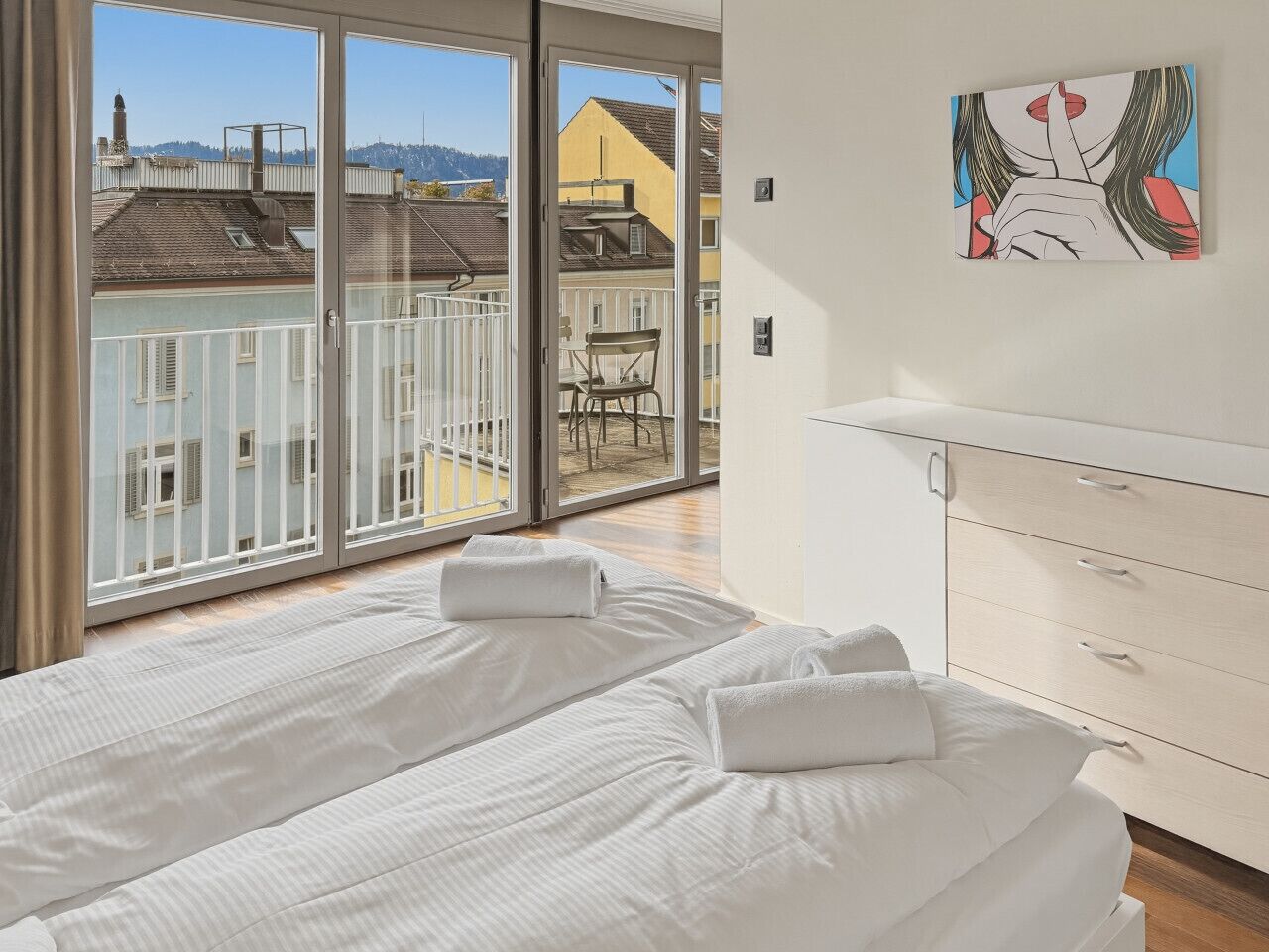 Une chambre d’hôtel avec un balcon, deux lits, une commode blanche et un tableau au mur.