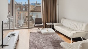 A modern living room with a white sofa, a glass coffee table, a chair, and a TV. - Comfortable 1BR flat / great location - Baron 44 (Zürich)
