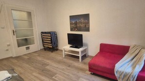 A room with a red sofa, a TV on a small table, a cityscape painting on the wall, and a door with frosted glass panels.