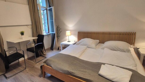 A hotel room with a bed, bedside tables, a desk, a chair, and a window with curtains.