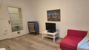 A room with a red sofa, a TV on a small table, a cityscape painting on the wall, and a door with frosted glass panels. - Charming 1BR Apt Near Central Vienna (Vienna)