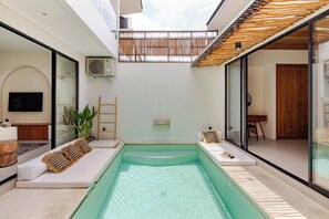 A modern indoor pool area with a clear view of the sky, a lounge area with seating, and a visible air conditioning unit.