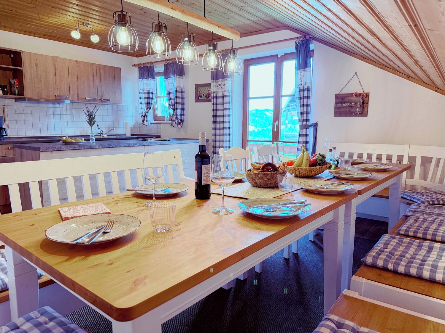 A dining area with a wooden table set for two, a bottle of wine, and a basket of bread.