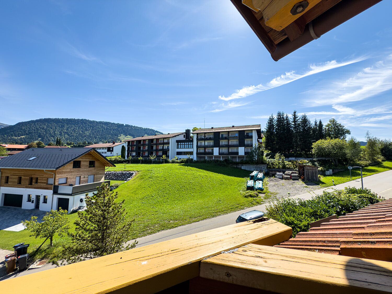 A residential area with a green lawn, a wooden deck, and a multi-story building with balconies.