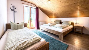 Ein gemütliches Schlafzimmer im Dachgeschoss mit zwei Betten, Holzbalkendecke und Blick durch ein großes Fenster.