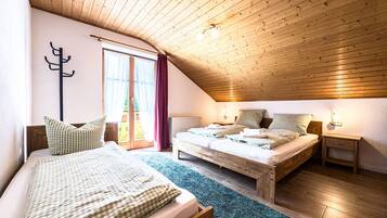 Ein gemütliches Schlafzimmer im Dachgeschoss mit zwei Betten, Holzbalkendecke und Blick durch ein großes Fenster.