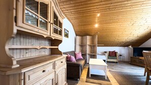Ein gemütliches Dachzimmer mit Holzbalken und -wänden, möbliert mit einer Couch, einem kleinen Tisch und einem Schrank.