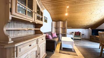 Ein gemütliches Dachzimmer mit Holzbalken und -wänden, möbliert mit einer Couch, einem kleinen Tisch und einem Schrank.