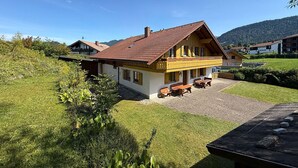 Eine zweistöckige Chalet mit rotem Ziegeldach, einem Balkon und einer Auffahrt mit Kies.