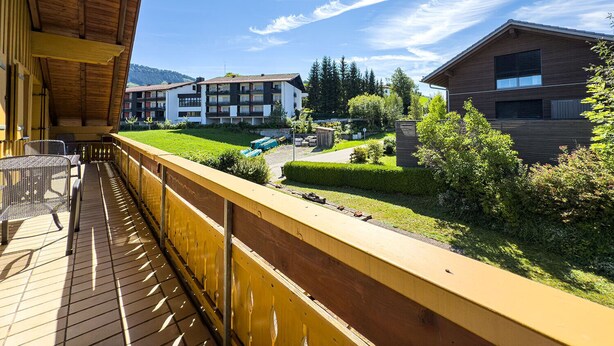 Ein Balkon mit Blick auf eine Wohngegend, darunter ein mehrgeschossiges Gebäude mit Balkonen und ein kleineres Holzhaus.
