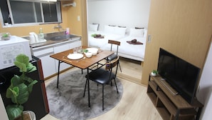 A compact living space with a kitchenette, a dining area, a sofa bed, and a television.