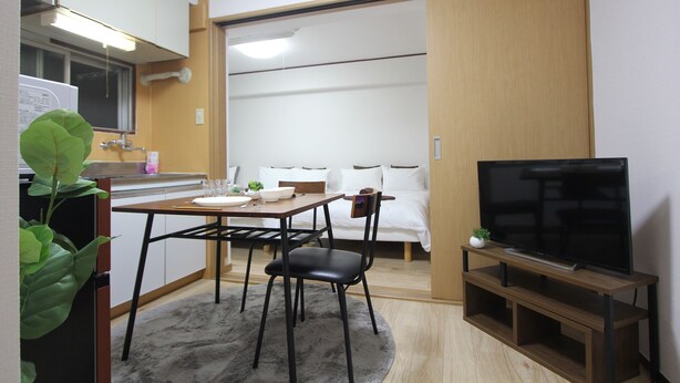 A compact living space with a kitchenette, a dining area, and a TV on a wooden stand.