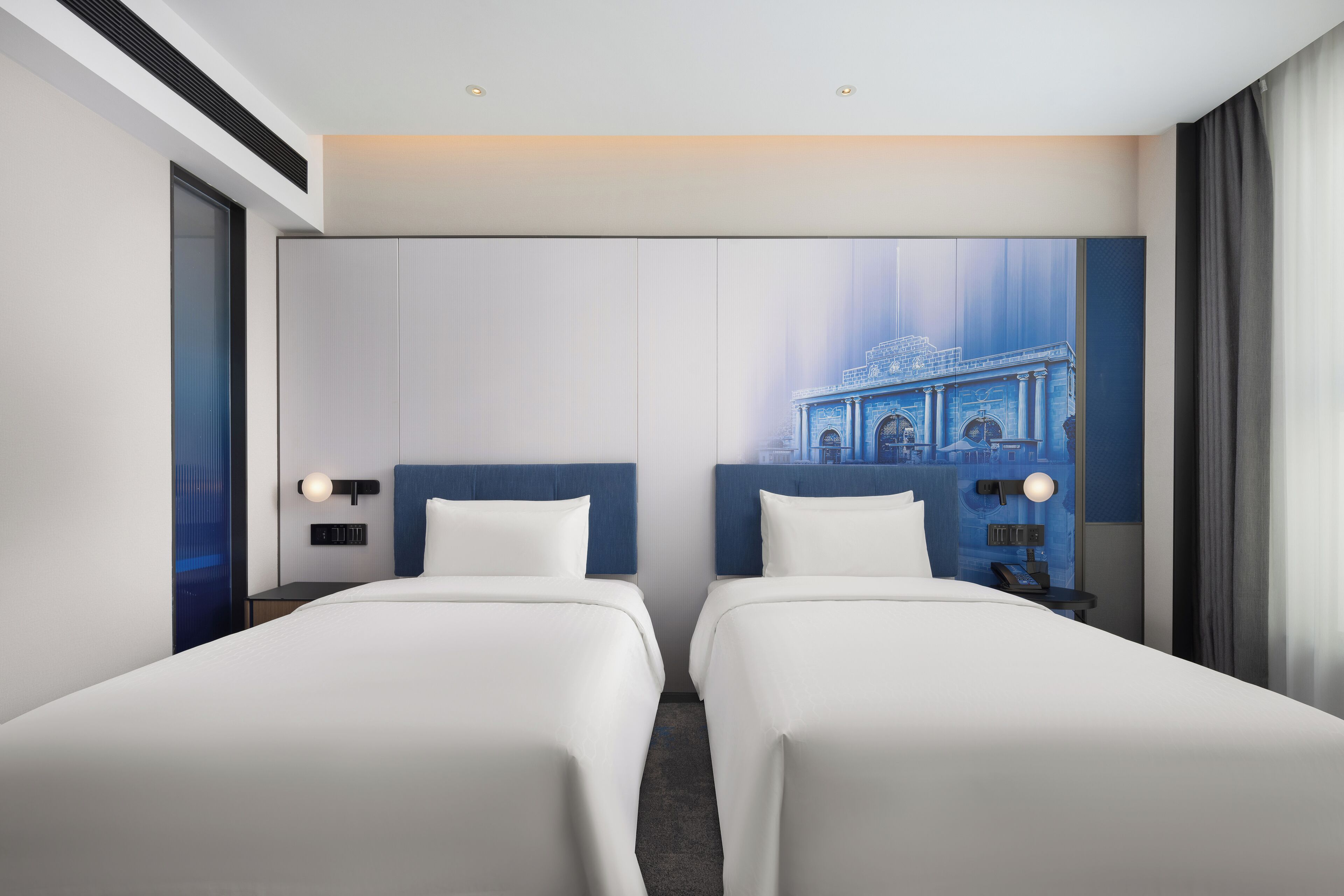 A hotel room with two beds, a large wall mural, and a cityscape view.