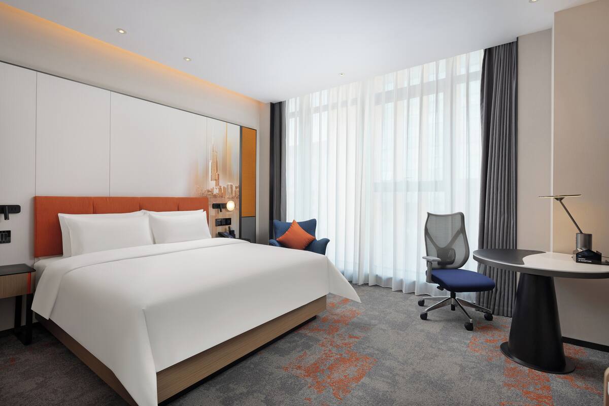 A modern hotel room with a large bed, a desk, and a chair.