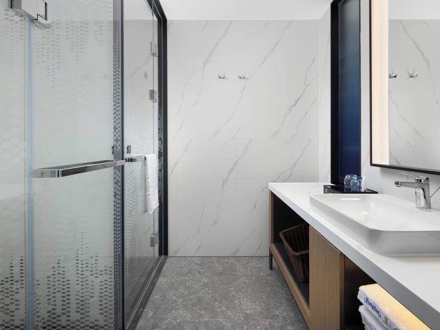 Un baño moderno con cabina de ducha de vidrio, un lavamanos blanco y un espejo grande.