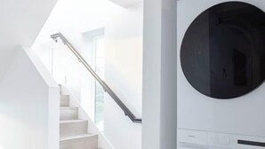Een modern interieur met een trap naar een lichte kamer, een wasmachine en een groot rond raam.