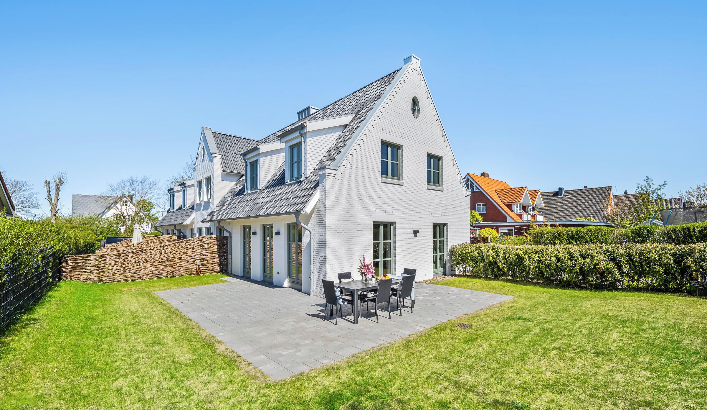 A modern two-story house with a patio, a dining area, and a well-maintained garden.