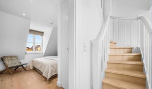 Een slaapkamer met een bed, een stoel, een raam en een trap.