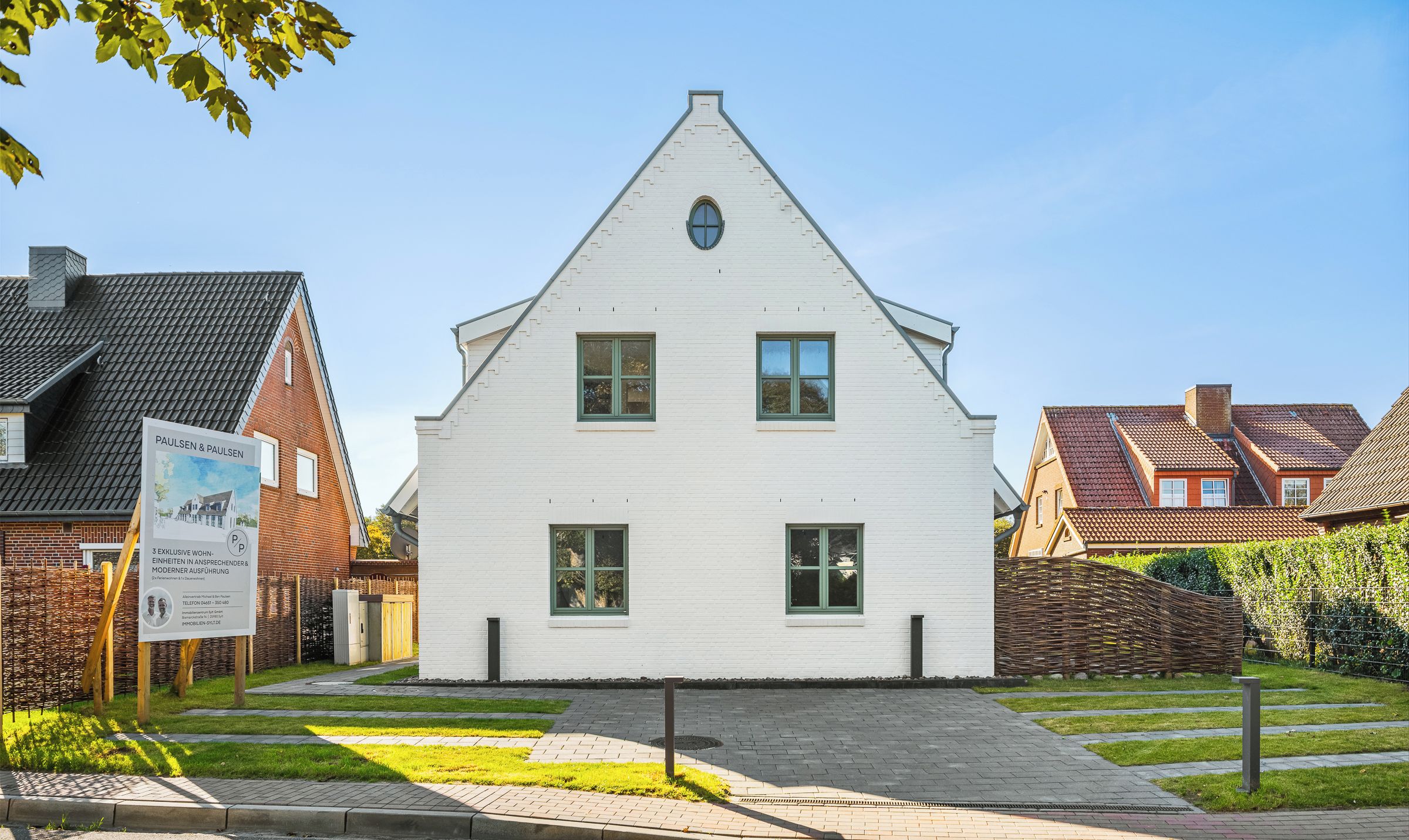 Une maison blanche avec un toit triangulaire, une allée pavée et un panneau indicateur.