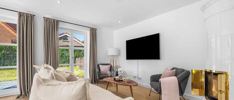 A modern living room with a sofa, a coffee table, a fireplace, a TV, and a view of the outdoors.