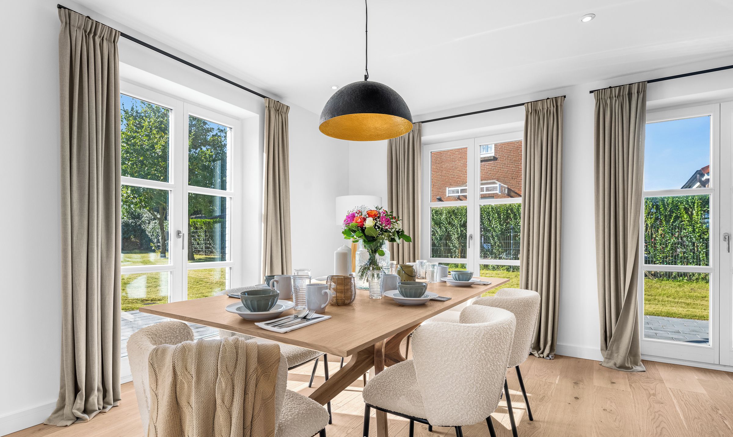 Et spiseområde med et træbord, beige stole og en sort pendellampe.