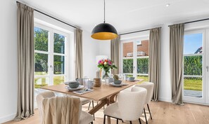 Een eethoek met een houten tafel, beige stoelen en een zwart hanglamp.