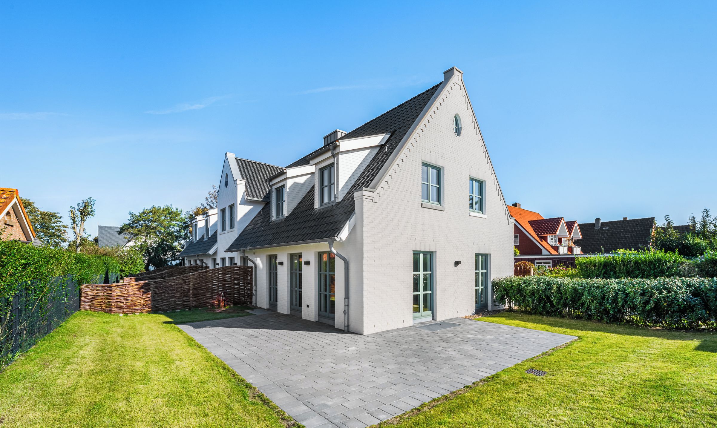 A modern two-story house with a sloped roof, a paved driveway, and a well-maintained lawn.