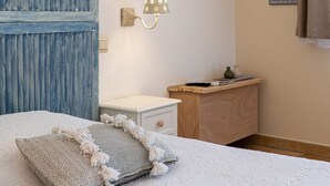 A bedroom with a bed, a nightstand, a dresser, a wall-mounted lamp, and a framed picture.