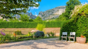 A gravel path, a metal fence, and two white chairs in a garden with a mountain backdrop.