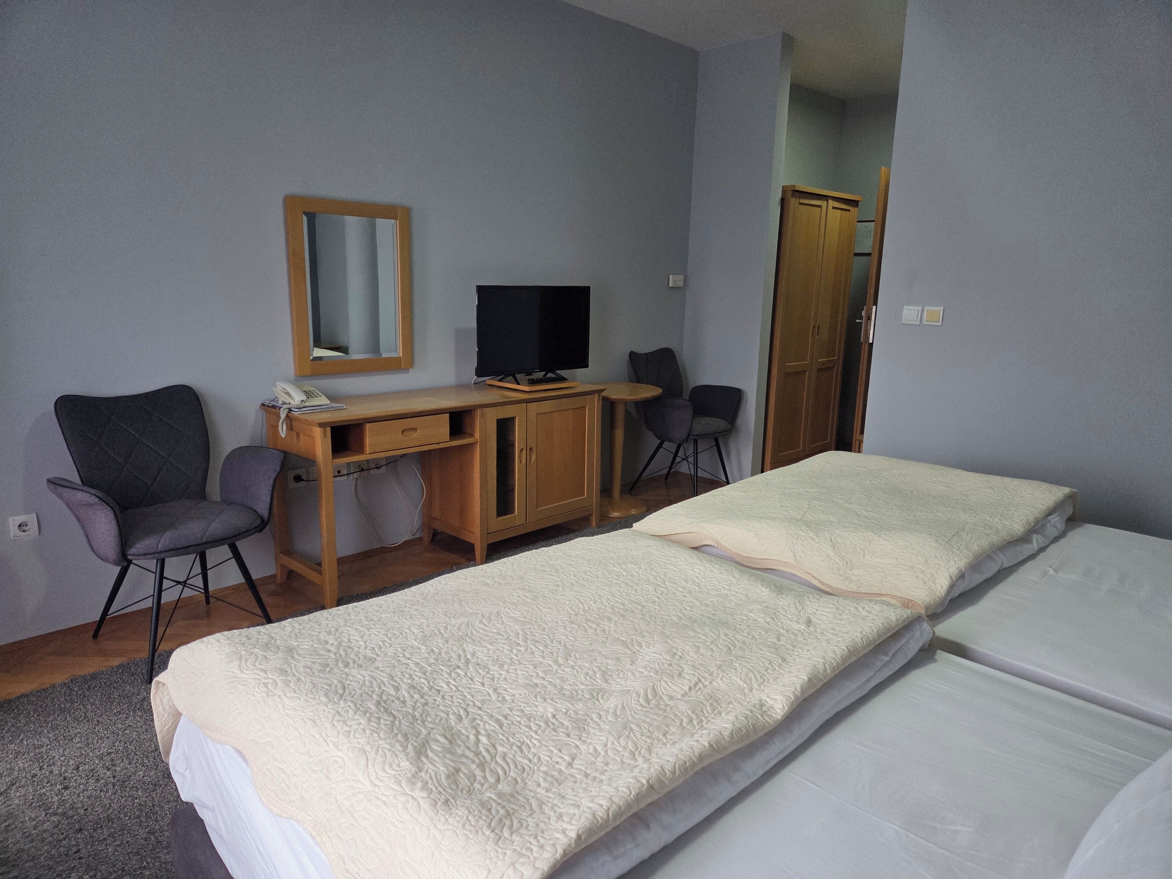 A hotel room with two beds, a desk with a computer, a chair, a wardrobe, and a mirror on the wall.
