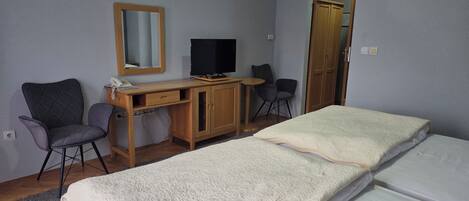A hotel room with two beds, a desk with a computer, a chair, a wardrobe, and a mirror on the wall.