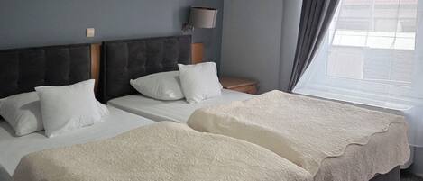 A hotel room with a large bed, two bedside tables, a lamp, a painting on the wall, and a window with curtains.