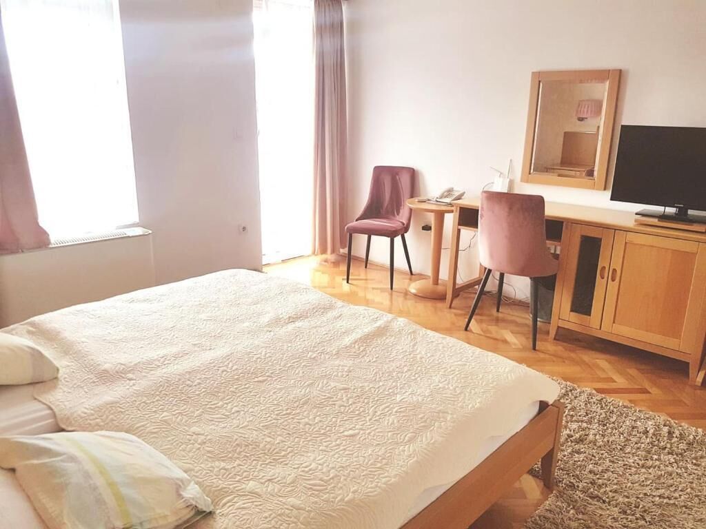 A hotel room with a large bed, a desk with a chair, a television, and a mirror.