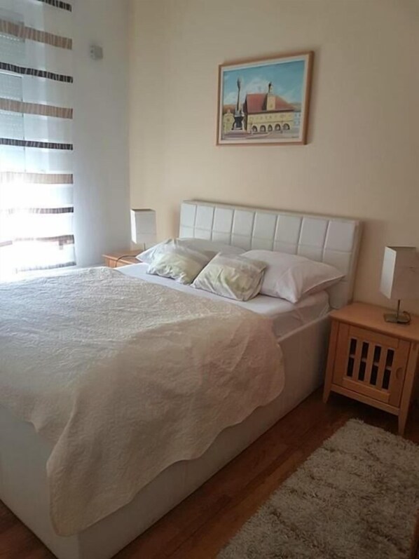 Un dormitorio con una cama grande, una mesita de noche, un cuadro en la pared y una ventana con persianas.