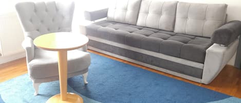 A living room with a grey sofa, a round wooden table, and a blue patterned rug.