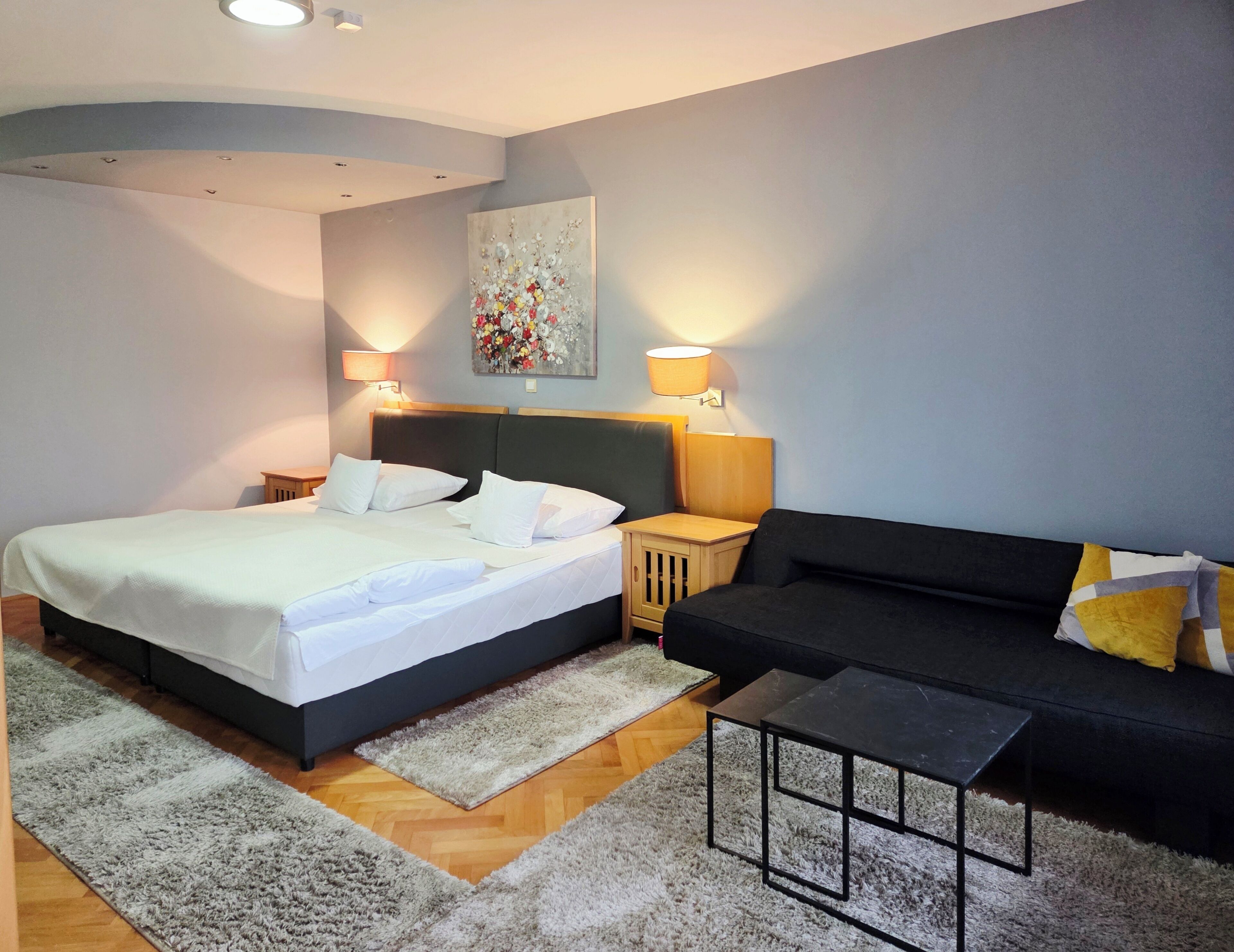 Un dormitorio moderno con una cama grande, un sofá negro, una mesita y dos lámparas de noche.
