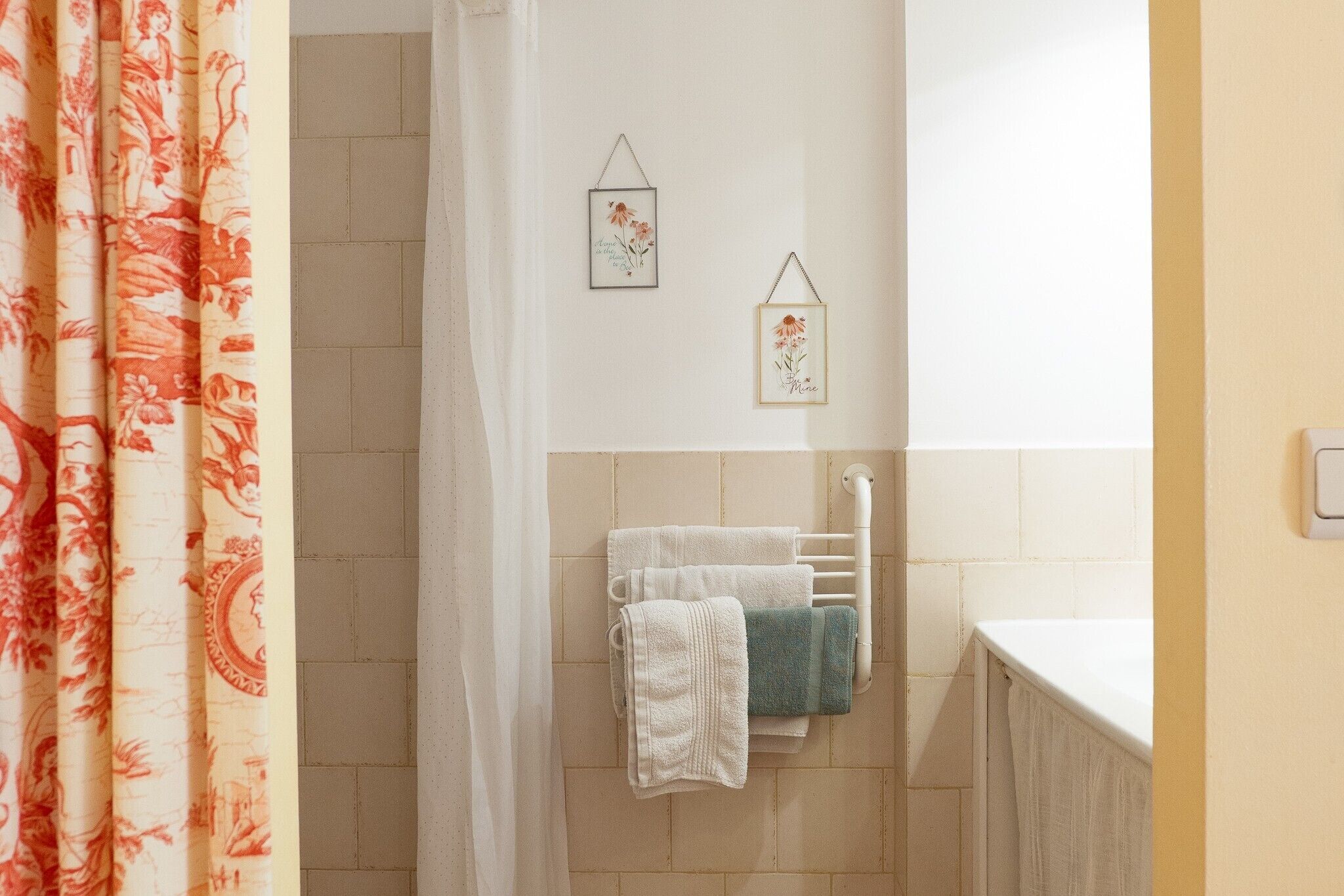 A bathroom with a towel rack, two framed pictures, and a shower curtain.