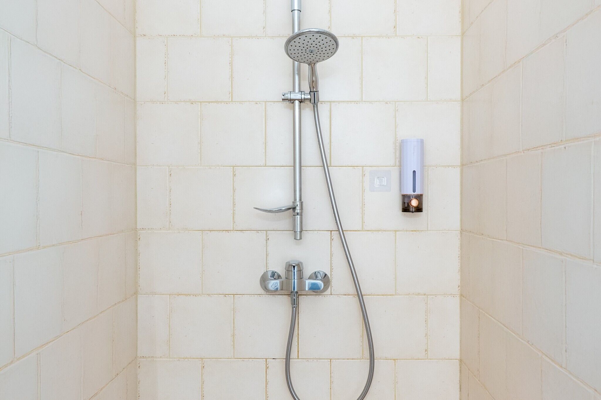 Une douche équipée d’un pommeau de douche à main et d’un robinet fixé au mur.