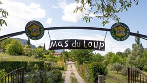 Ein Schild mit den Logos 'Mas du Loup' und 'Gites de France', ein Kiesweg und üppiges Grün.
