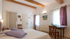 Ein Schlafzimmer mit einem Bett, zwei Stühlen, einem Schreibtisch und einem Fenster mit Vorhängen.