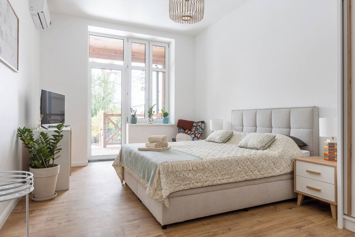 A bedroom with a bed, bedside table, TV, and potted plants.