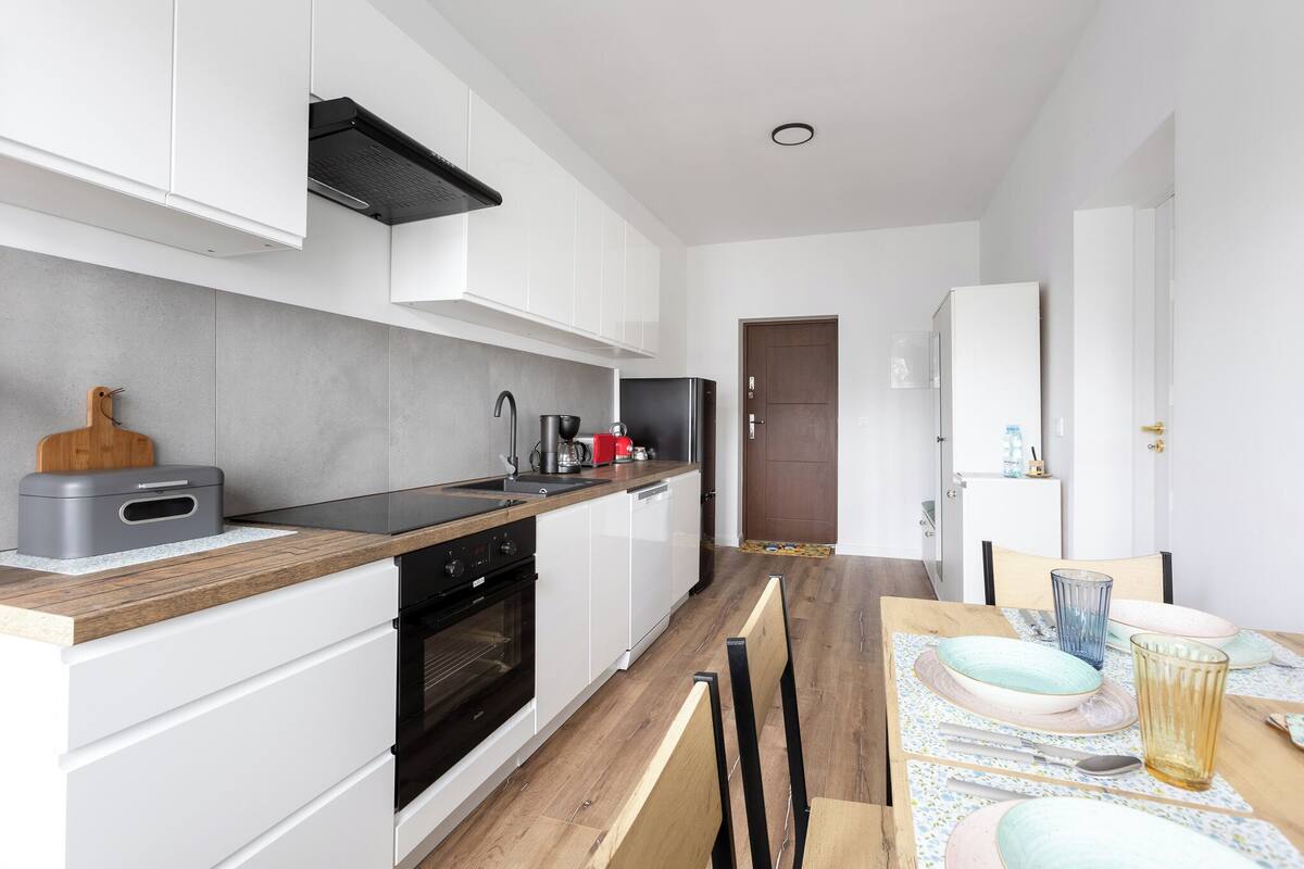 A modern kitchen with white cabinets, a black stove, and a wooden countertop.