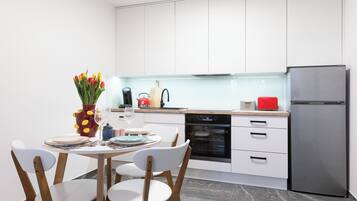 A modern kitchen with white cabinets, a stainless steel refrigerator, and a dining area with white chairs and a table set for two.