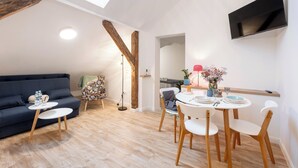 A modern living room with a sofa, two small tables, a dining table with chairs, a TV mounted on the wall, and a skylight. - Apartamenty Stare Bielsko (Bielsko-Biała)