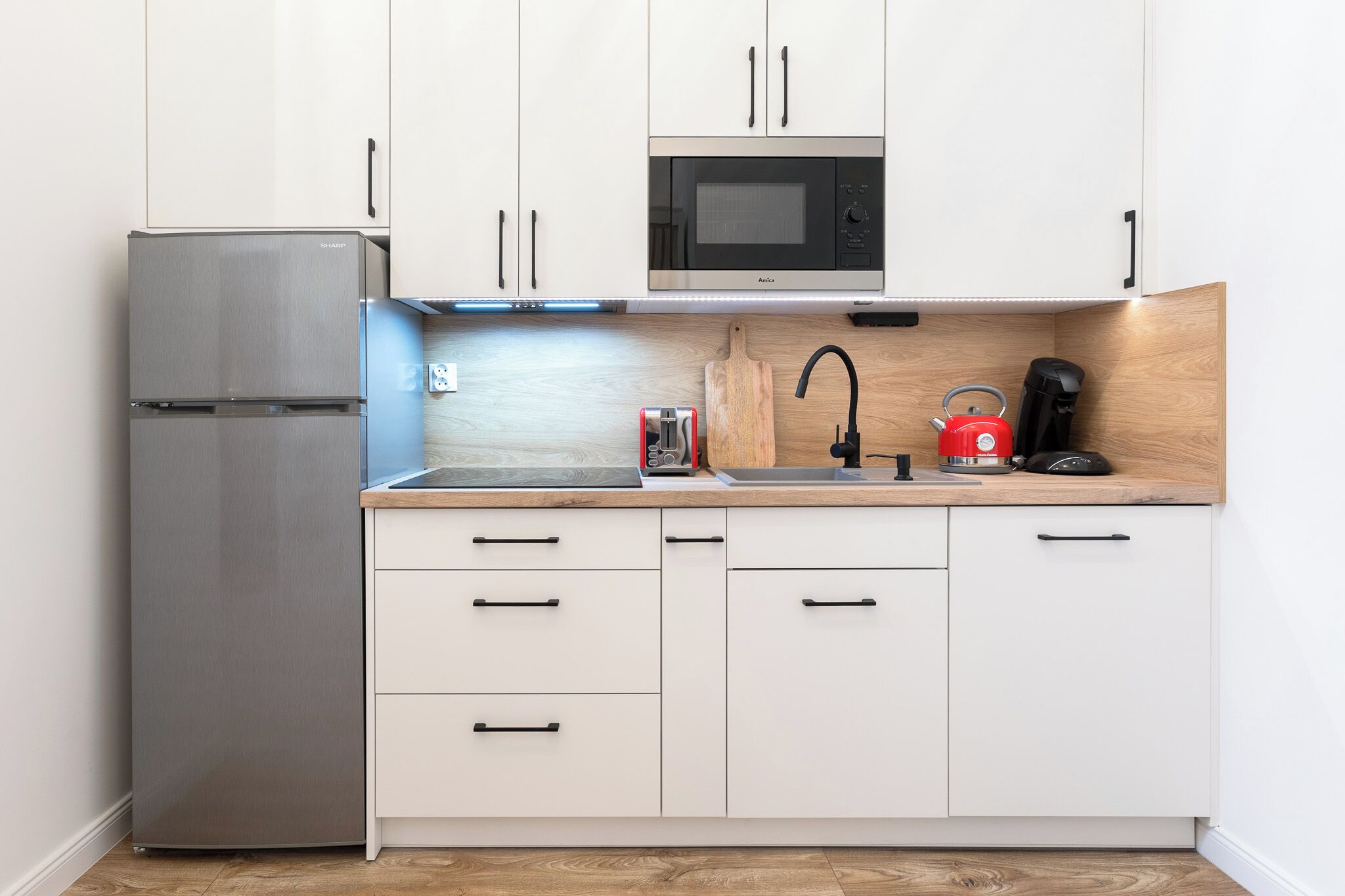 A compact kitchen with a stainless steel refrigerator, a microwave, a sink, and a coffee maker.