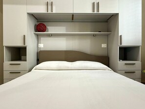Ein Schlafzimmer mit einem Bett, einem Kopfteil, zwei Nachttischen und einem Regal über dem Bett.