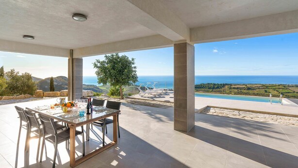 A covered outdoor dining area with a table set for two, overlooking a pool and a scenic view of the ocean. - Villa Lily with private pool - My Rental Homes (Montallegro)