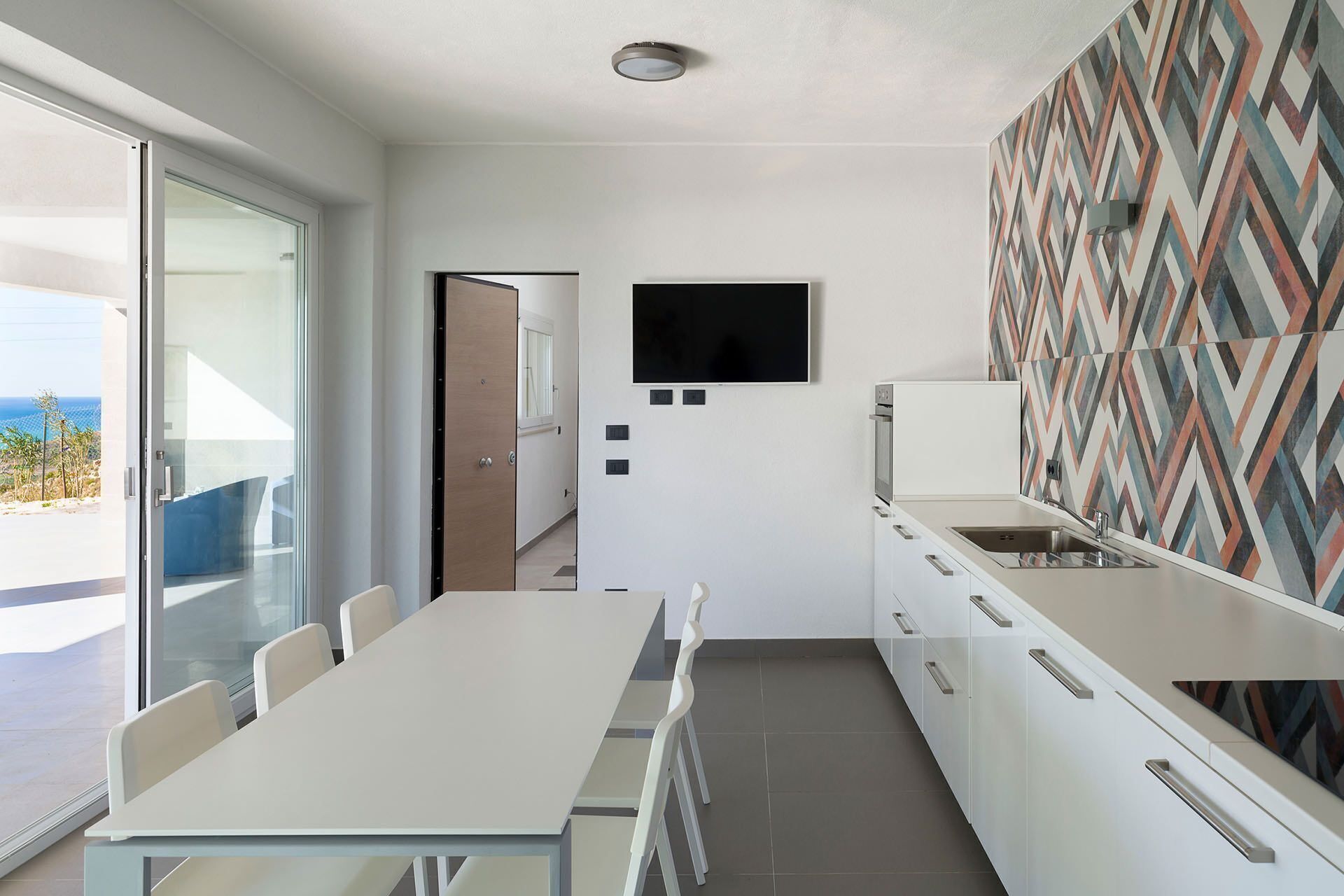 Une cuisine moderne dotée d’un grand îlot central, d’un téléviseur à écran plat fixé au mur et d’un crédence décorée de motifs.